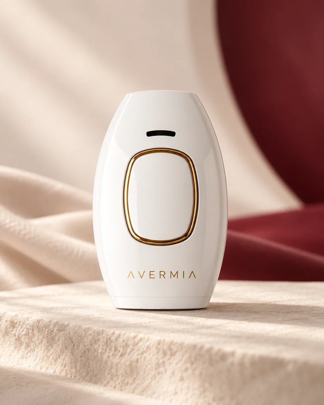AVERMIA IPL handset on an ivory surface with burgundy fabric, illustrative product photograph.